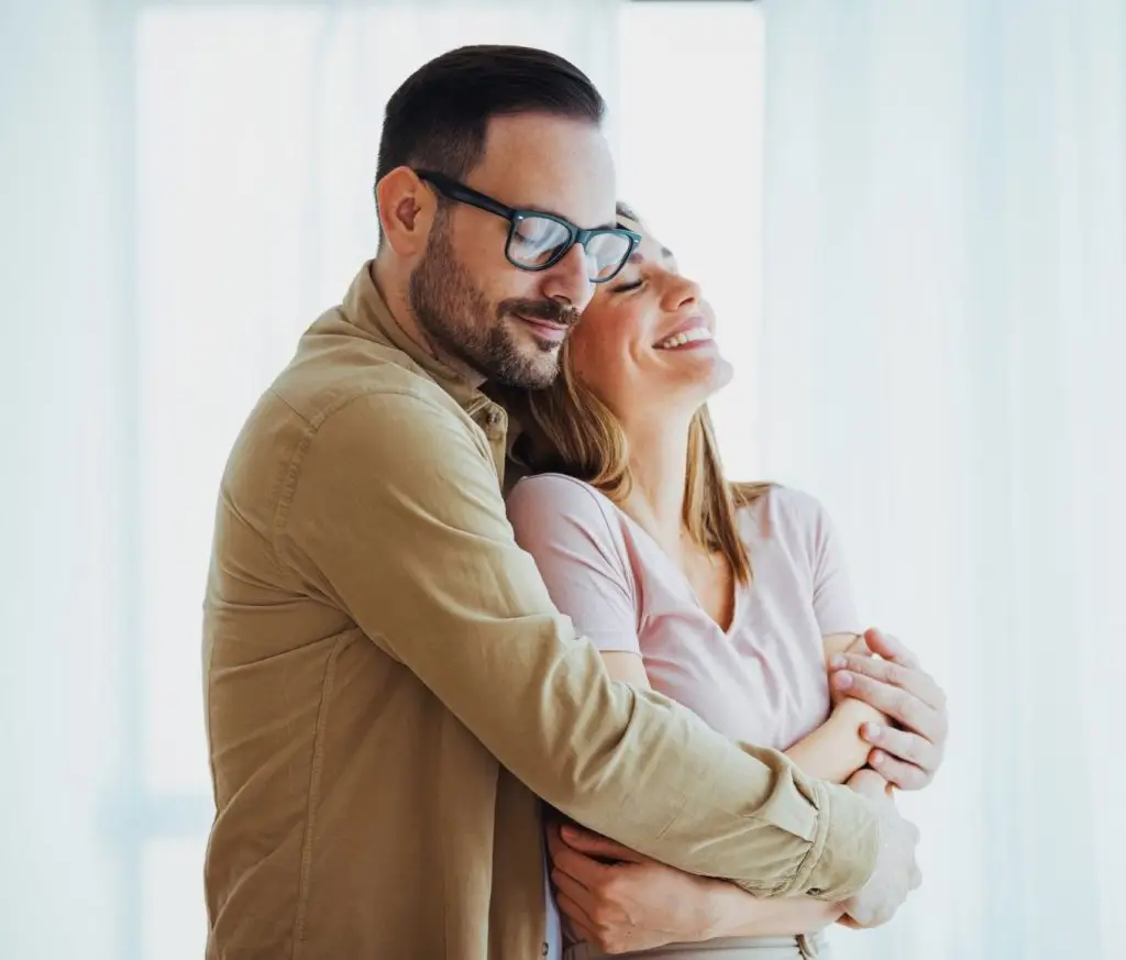 Cheerful young couple looking outside window. Portrait of smiling couple thinking about the future. Happy cheerful couple relaxing at home.