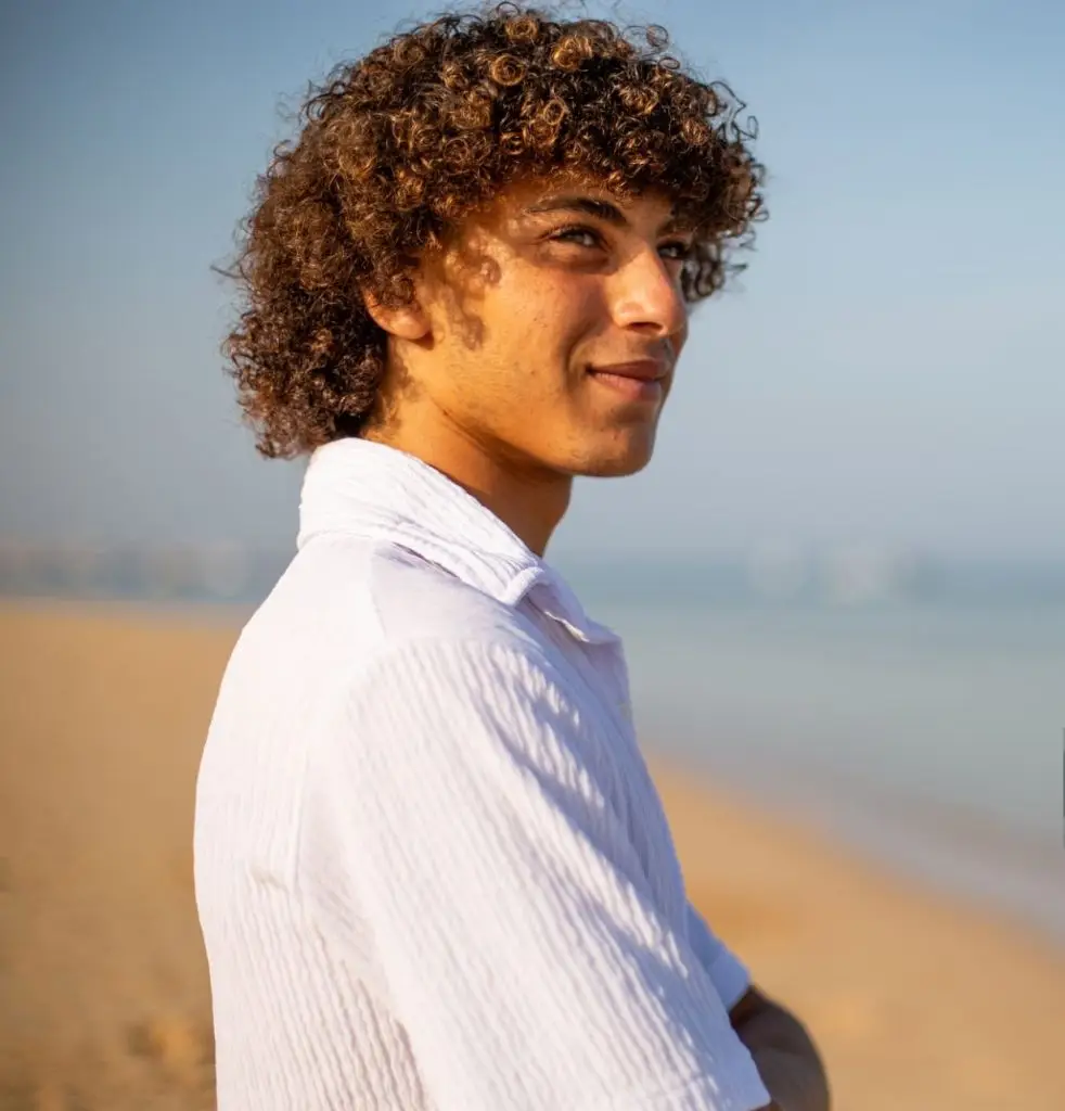 Young man with curly hair standing on beach, enjoying nature and serene view